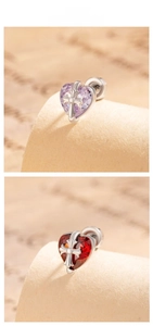 Macro detail of heart-shaped earrings with gothic cross overlay and vibrant crystals