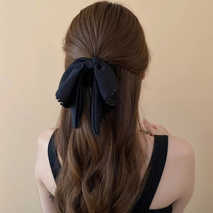 Detail showing a black bow hair claw with bead trim styled on long wavy hair