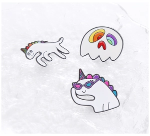 Detailed view of three enamel pins featuring a dinosaur, ghost, and unicorn on ice