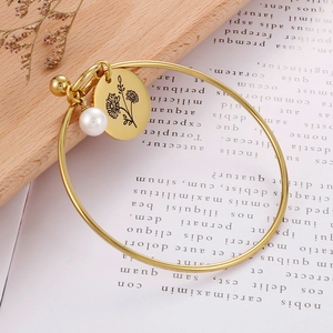 Goldenes Geburtsblumenarmband mit weißer Perle auf rustikalem Holz- und Papierhintergrund