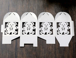 Detailed view of white laser-cut teddy bear candy box flat lay on wooden surface