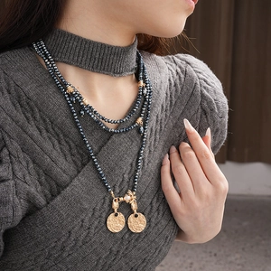 Detail of vintage gold layered long necklace with insect pendant and grey beads on a sweater