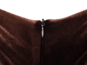 Macro view of hidden zipper detail on brown velvet pleated midi dress fabric