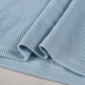 Detailed macro view of light blue waffle knit fabric texture and hemline stitching quality