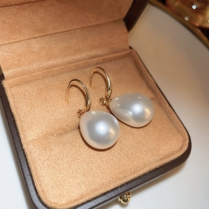 Macro shot of elegant white teardrop pearls with golden hooks on a brown velvet base