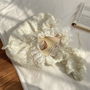 Close-up of floral bag with lace trim, ruffles, and ribbon detail on a white bed sheet
