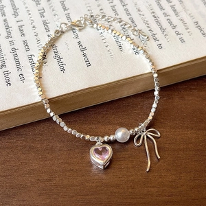 Silbernes Armband mit rosa Herz-Zirkon und Perle auf einem eleganten Buchhintergrund