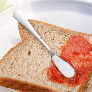 Couteau à beurre en acier inoxydable étalant de la confiture rouge sur du pain grillé