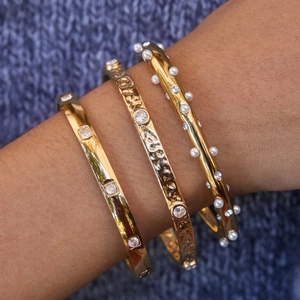 Macro shot of three stacked 18k gold-plated bangles with pearls and cubic zirconia stones