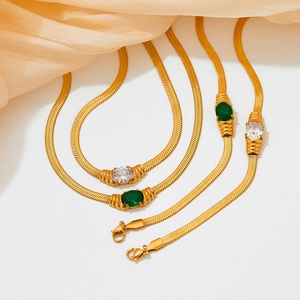 Gold snake chain necklaces with green and clear oval gemstones on orange silk fabric