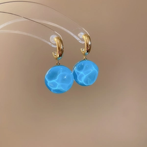 Détail des boucles d'oreilles en verre bleu clair à effet d'eau et crochets dorés