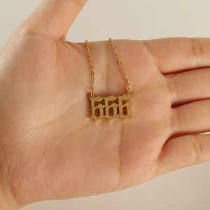 Golden stainless steel necklace with matte finish 666 pendant held in hand for scale