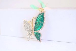 Macro detail of a gold butterfly keychain featuring white rhinestones and green enamel