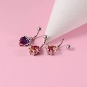 Detail of silver heart-shaped belly rings with colorful gemstones on a pink backdrop