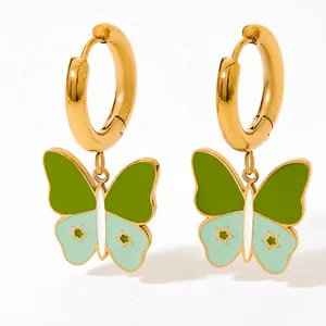Détail de boucles d'oreilles créoles dorées avec pendentifs papillon vert et étoiles