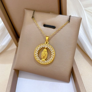 Detailed close-up of a gold Virgin Mary pendant with cubic zirconia on beige jewelry cushion