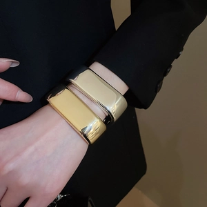 Close-up of minimalist gold wave bangle bracelets paired with a sleek black blazer suit