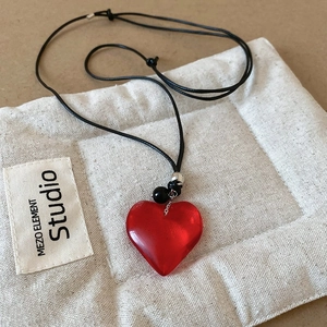 Close-up of a vintage red resin heart pendant on a black cord necklace with silver beads