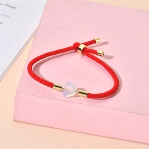 Detail of red braided rope bracelet with heart stone and adjustable gold metal clasp