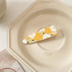 Detailed close-up of yellow and white flower acrylic hair clip on ceramic plate