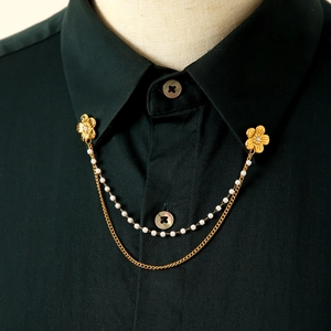 Dettaglio della spilla a fiore dorata con catene di perle su un colletto di camicia