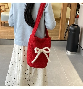 Red plush bucket bag with white bow knot detail shown as crossbody on model in cafe