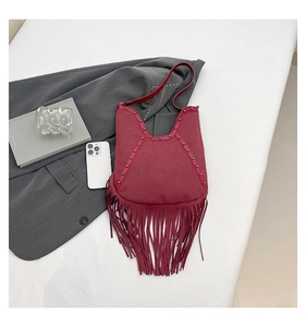 Detail of burgundy tassel bag with sun totem carving and stud decoration on a white background