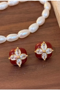 Macro shot of red floral stud earrings with gold plating and zircon center on wood