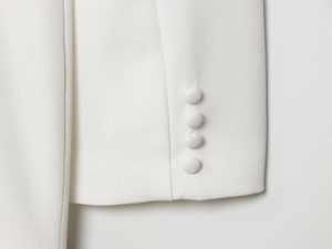 Détail de la manche d'un blazer blanc avec quatre boutons recouverts et texture raffinée