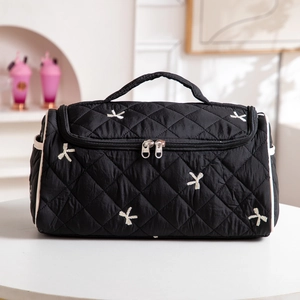 Detail of black quilted makeup bag with white bow embroidery and double zippers
