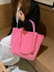Dettaglio della borsa tote in peluche rosa con decoro a cuore su panca di legno