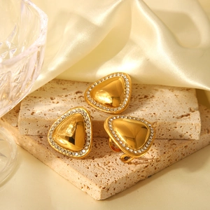 Macro view of three gold triangle stud earrings with shimmering rhinestones on silk