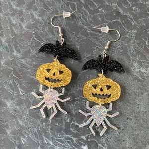 Halloween acrylic drop earrings with glitter bat, pumpkin, and spider charms on marble background