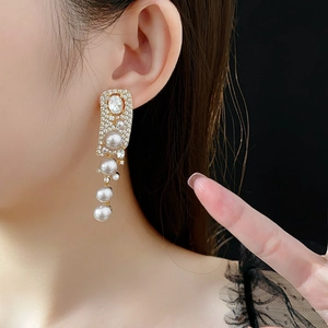 Close-up of elegant long tassel earrings with white pearls and crystals on a model