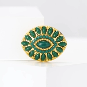 Macro shot of vintage gold brooch with dark green central gem and beaded oval border