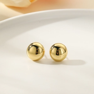 Macro detail of high-polish 18k gold plated spherical stud earrings on a white tray