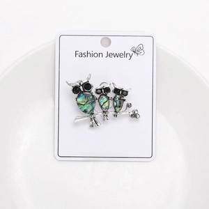 Macro detail of three vintage owl brooches with abalone shell inlay on display card