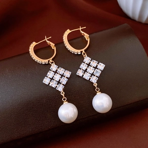Détail macro de boucles d'oreilles en or 18k avec pendentif en zircon et perle blanche