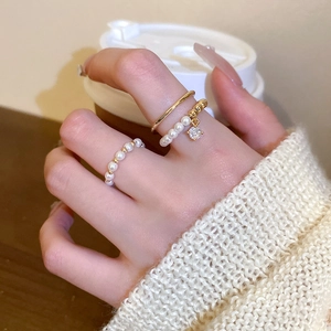 Set of 3 gold-plated rings with pearls and zircon pendant worn by a model in warm light