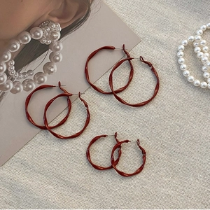 Three pairs of vintage dark red twisted geometric hoop earrings on a beige textured cloth
