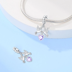 Dettaglio dello charm con due uccelli e cuore viola su un braccialetto d'argento