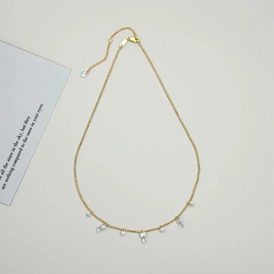 Close-up of golden olive branch necklace with zircon pendants on a minimalist white background