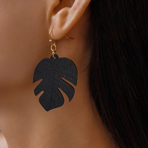 Close-up of model wearing black Monstera leaf earrings with gold hooks for resort style