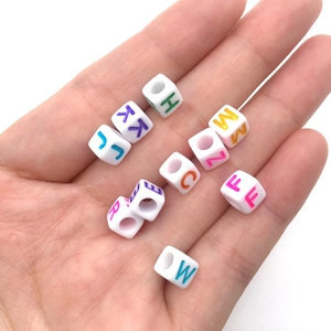 Close-up of white acrylic cube beads with colorful letters held in a palm for DIY
