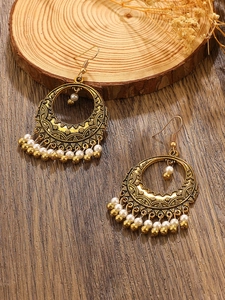 Detail of vintage bohemian hoop earrings with carved gold finish and white bead tassels