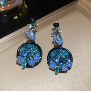 Dettaglio degli orecchini pipa a fiore blu con pietre scintillanti e smalto su cofanetto