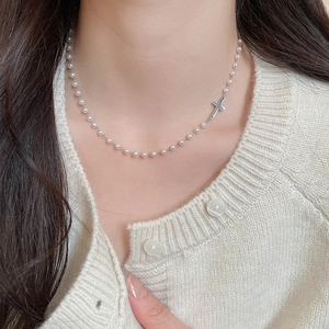 Close-up of pearl necklace with silver cross pendant worn by model over knitwear