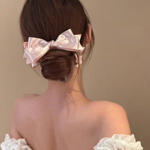 Pink satin bow hair clip with black polka dots shown on elegant woman hairstyle