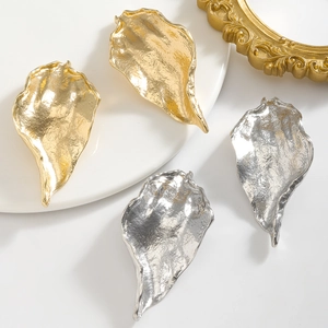Macro detail of abstract leaf earrings with hammered metal texture in gold and silver