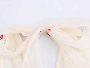 Detail of a beige chiffon bow with delicate red floral embroidery on a summer dress